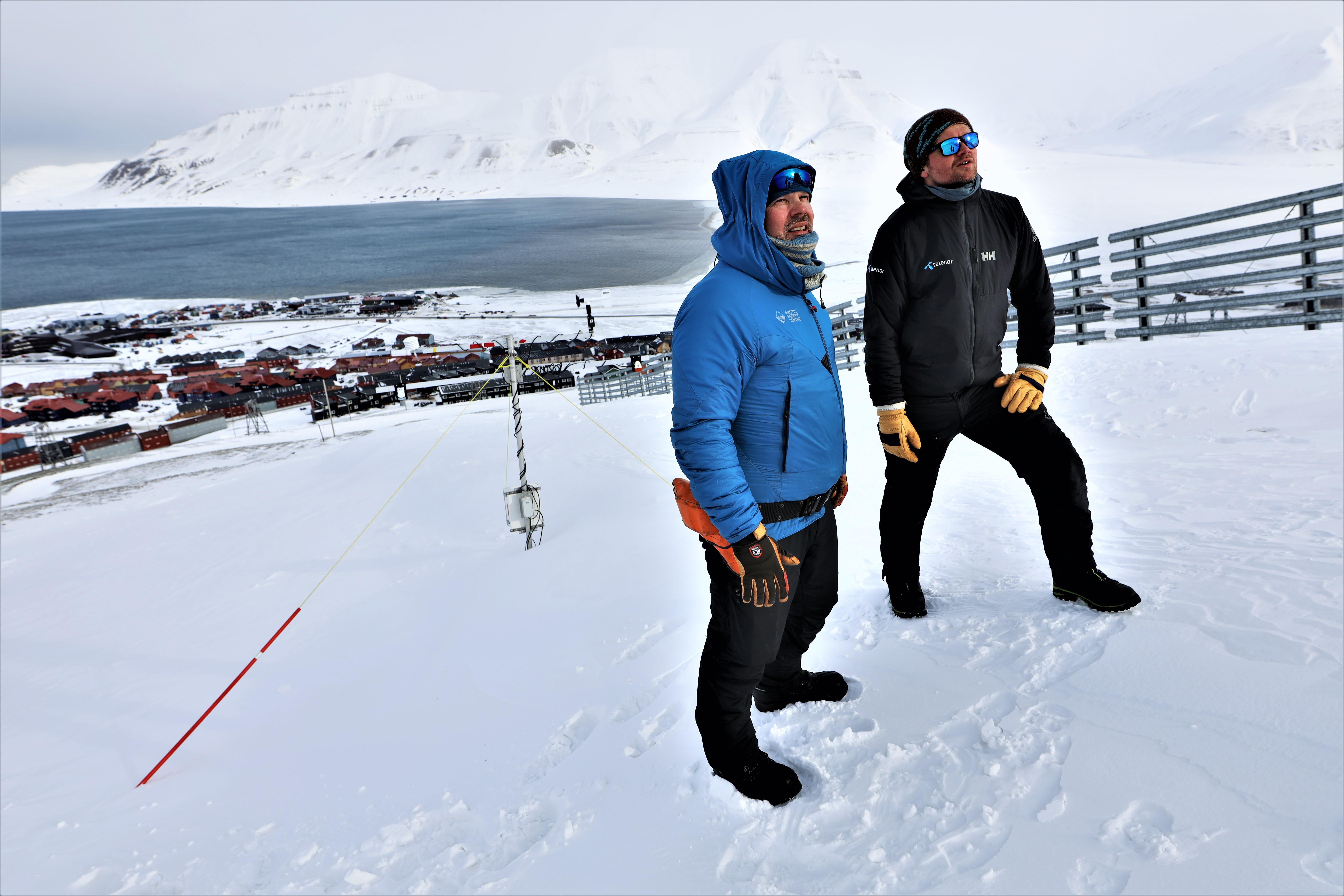 Two men standing on hillside looking towards the mountain peak.